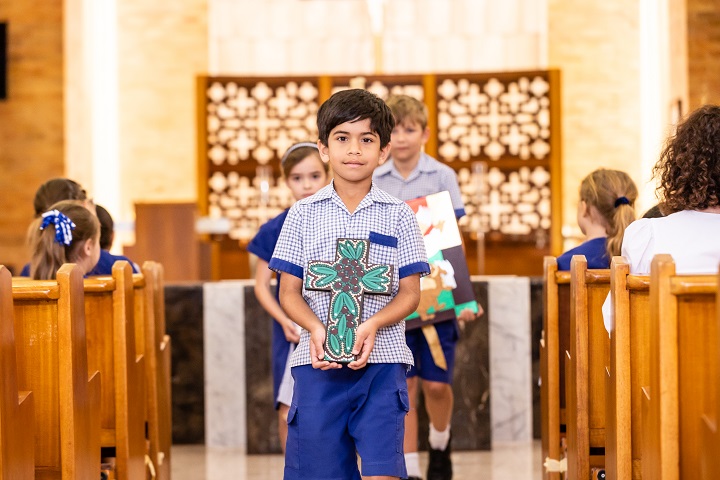 Student carrying a decorated cross during a school liturgy in a church.
