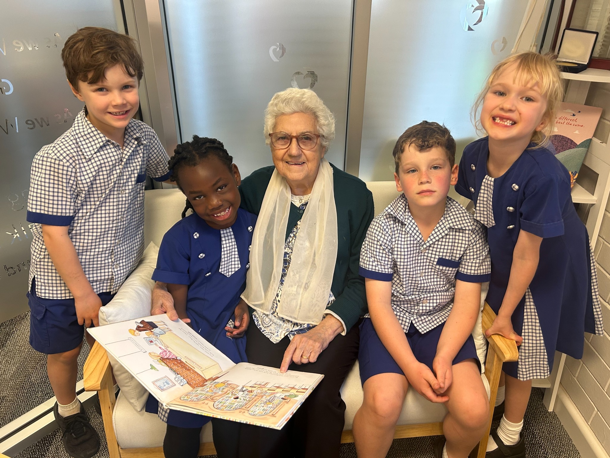 Students listening as an older adult reads a book during a shared reading activity.