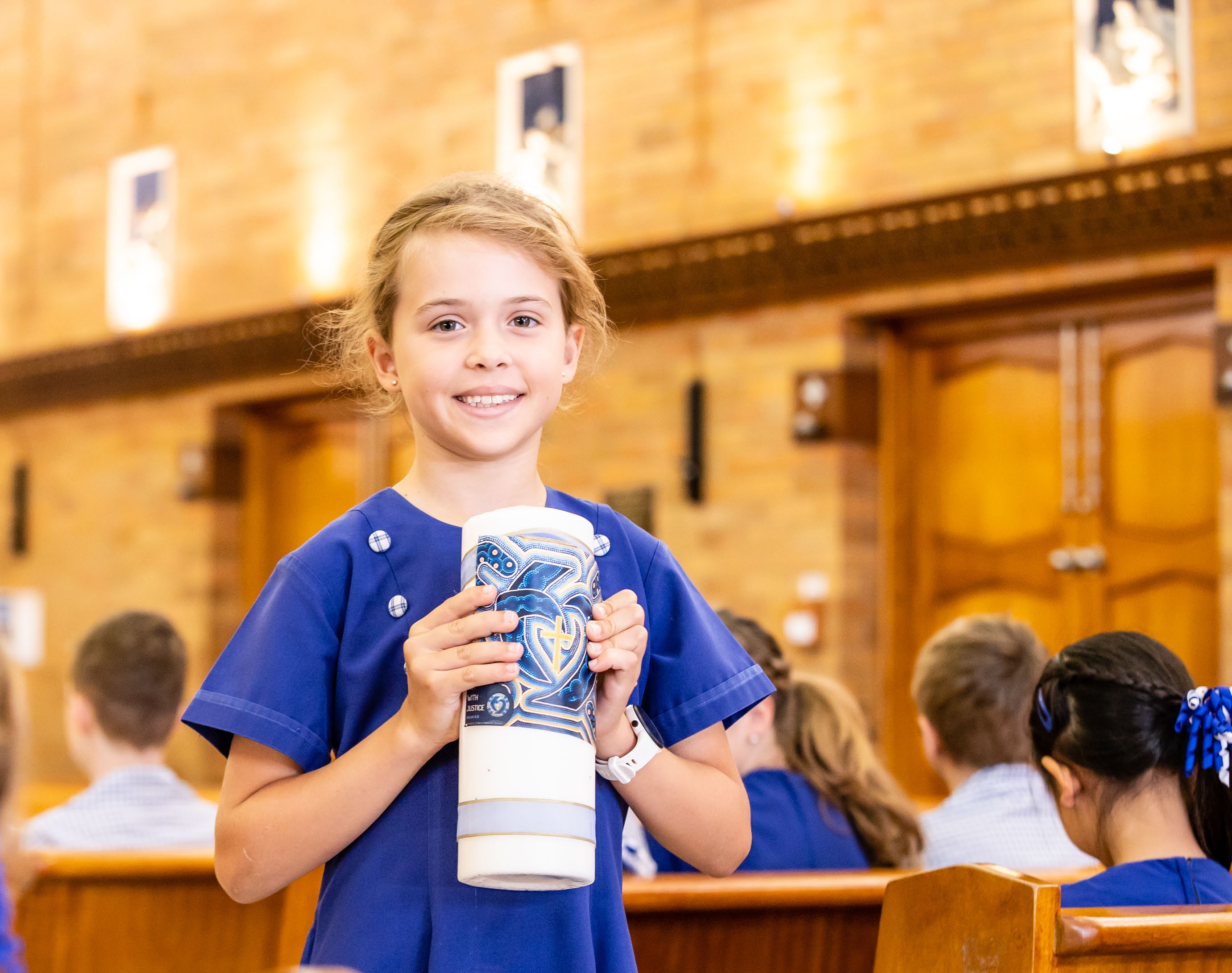 Student holding a decorated candle during a school liturgy in a church.